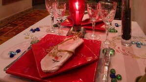 A dining table set with red plates, clear glasses, and a vase with a rose. - Riad Bab Tilila (Marrakech)