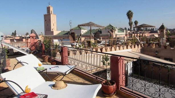 A rooftop terrace with lounge chairs, potted plants, and a view of a tower and buildings. - Riad Bab Tilila (Marrakech)