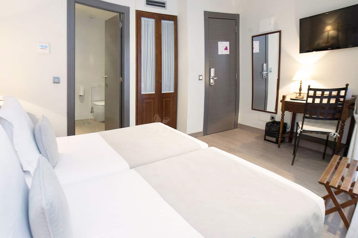 Une chambre d’hôtel comprenant un lit, un bureau avec une chaise, une télévision et une porte donnant sur une salle de bain.