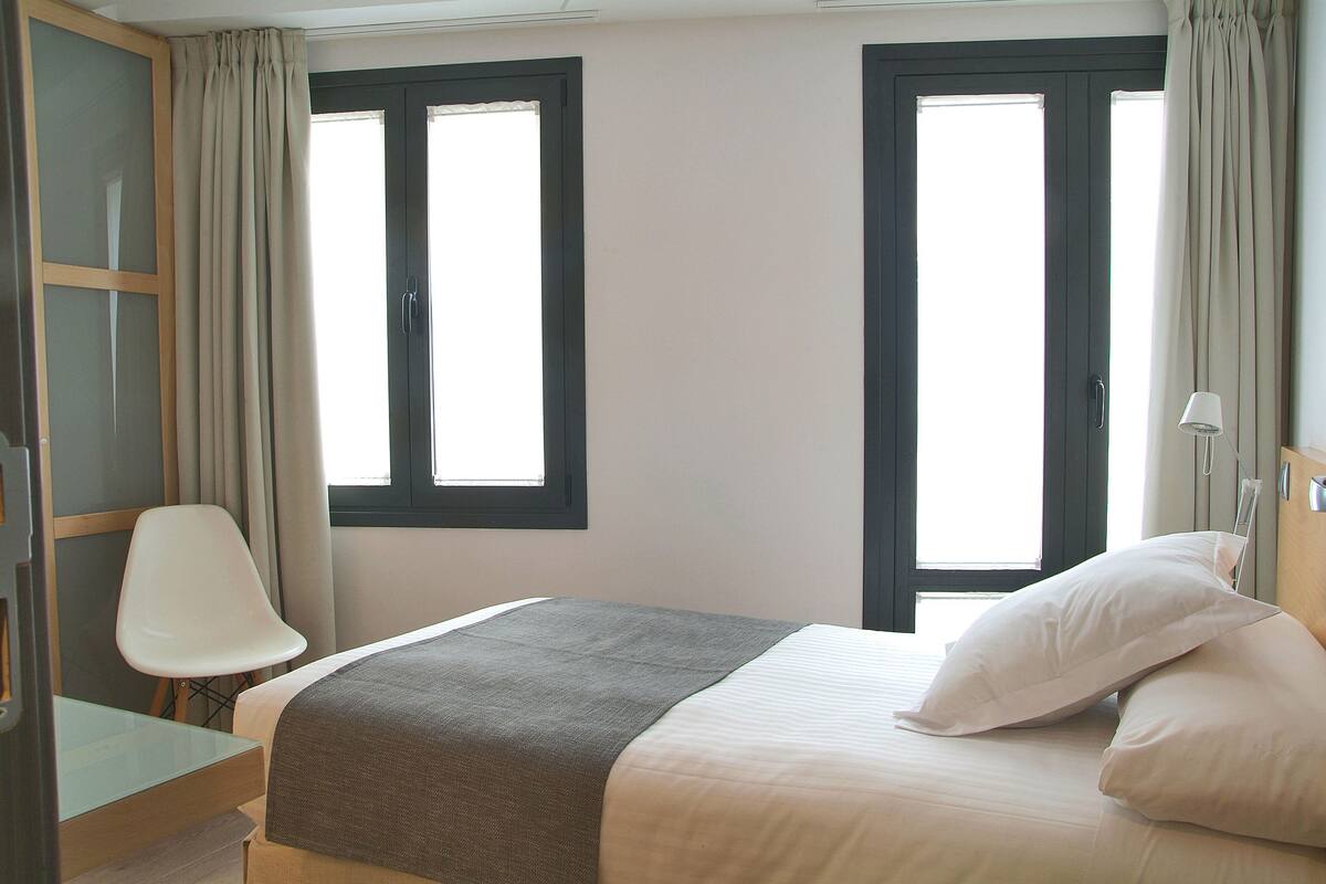Une chambre à coucher avec un lit, une chaise, deux fenêtres et une armoire.