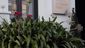 Een bordje voor 'le petit boutique hotel' met een raam en planten op de voorgrond.