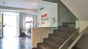Een modern hotelinterieur met een trap, een receptiebalie en een bord waarop staat 'le petit boutique hotel'.