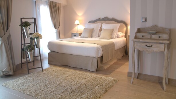 Een slaapkamer met een groot bed, nachtkastjes, een kaptafel, een lamp, een dressoir en een plantenstandaard.