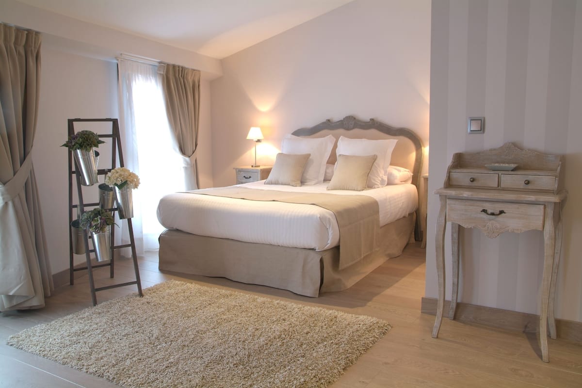 Une chambre à coucher avec un grand lit, des tables de chevet, une commode, une lampe, une coiffeuse et un support pour plante.