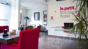 Een moderne hotel lobby met een glazen tafel, rode stoelen, een laptop op de tafel en een bordje met de tekst 'le.petit. boutique hotel'.