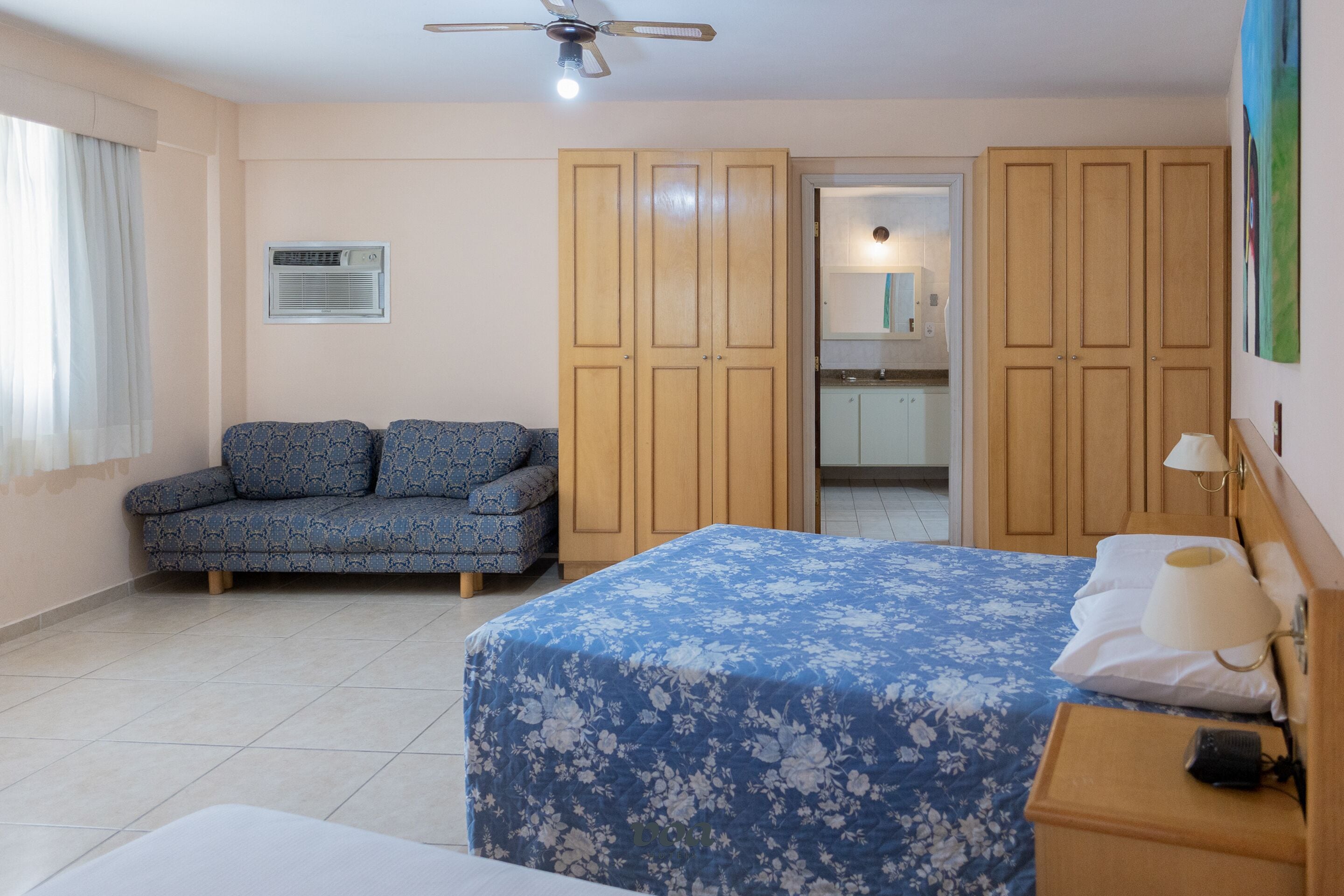 Una habitación de hotel con cama, sofá, armario y ventilador de techo.