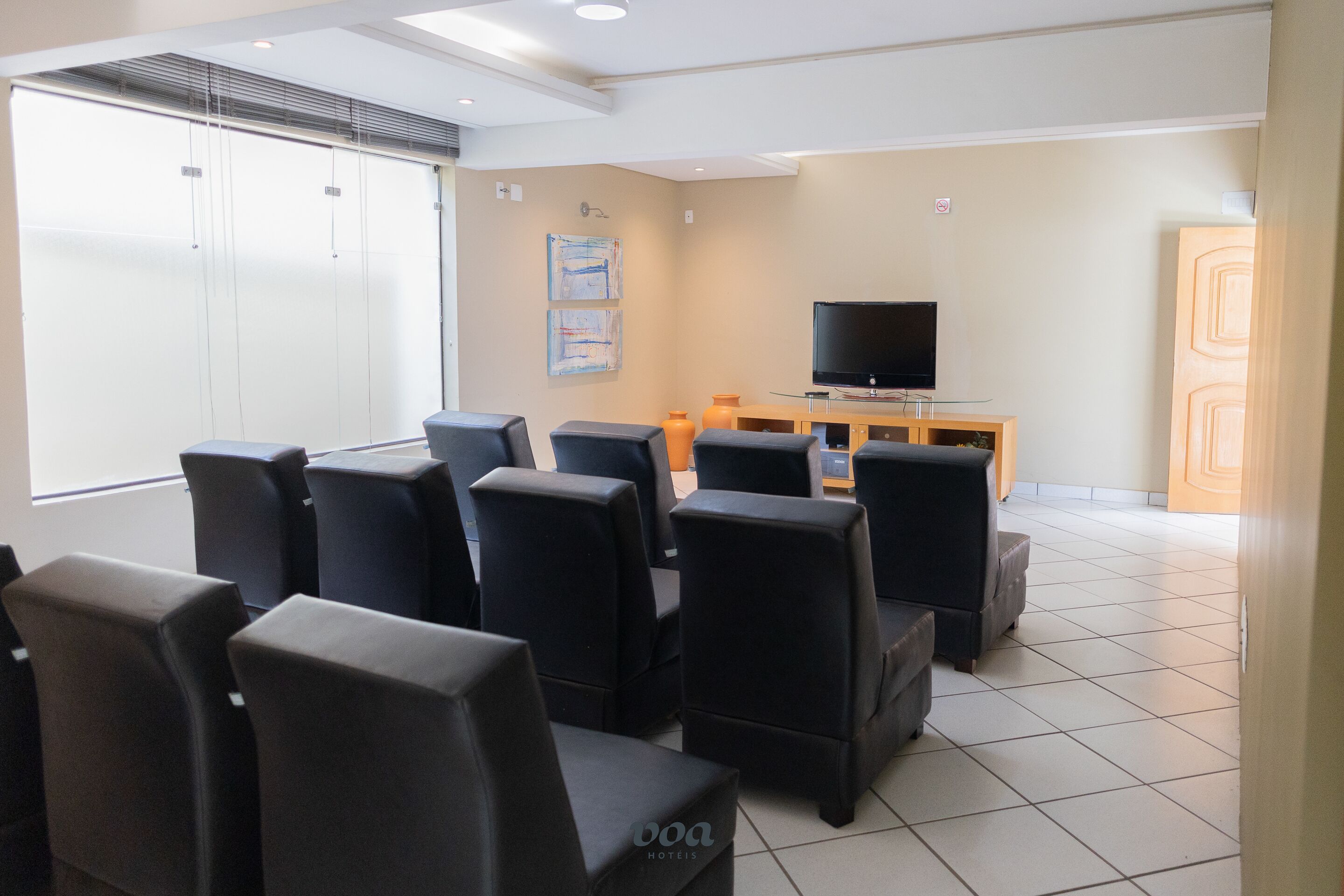 A hotel room with a seating area, a television on a wooden stand, and a large window.