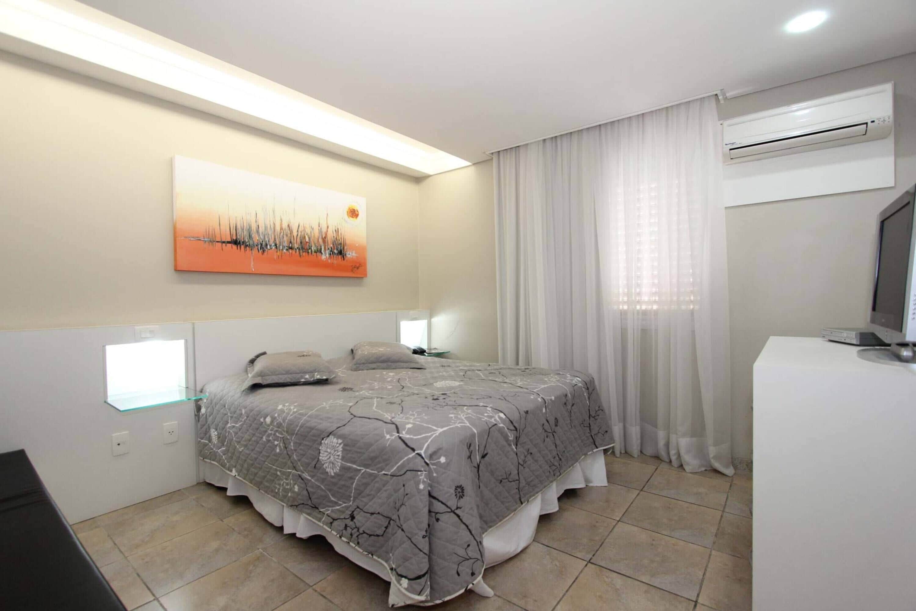 A bedroom with a bed, a bedside table, a TV, and an air conditioning unit.