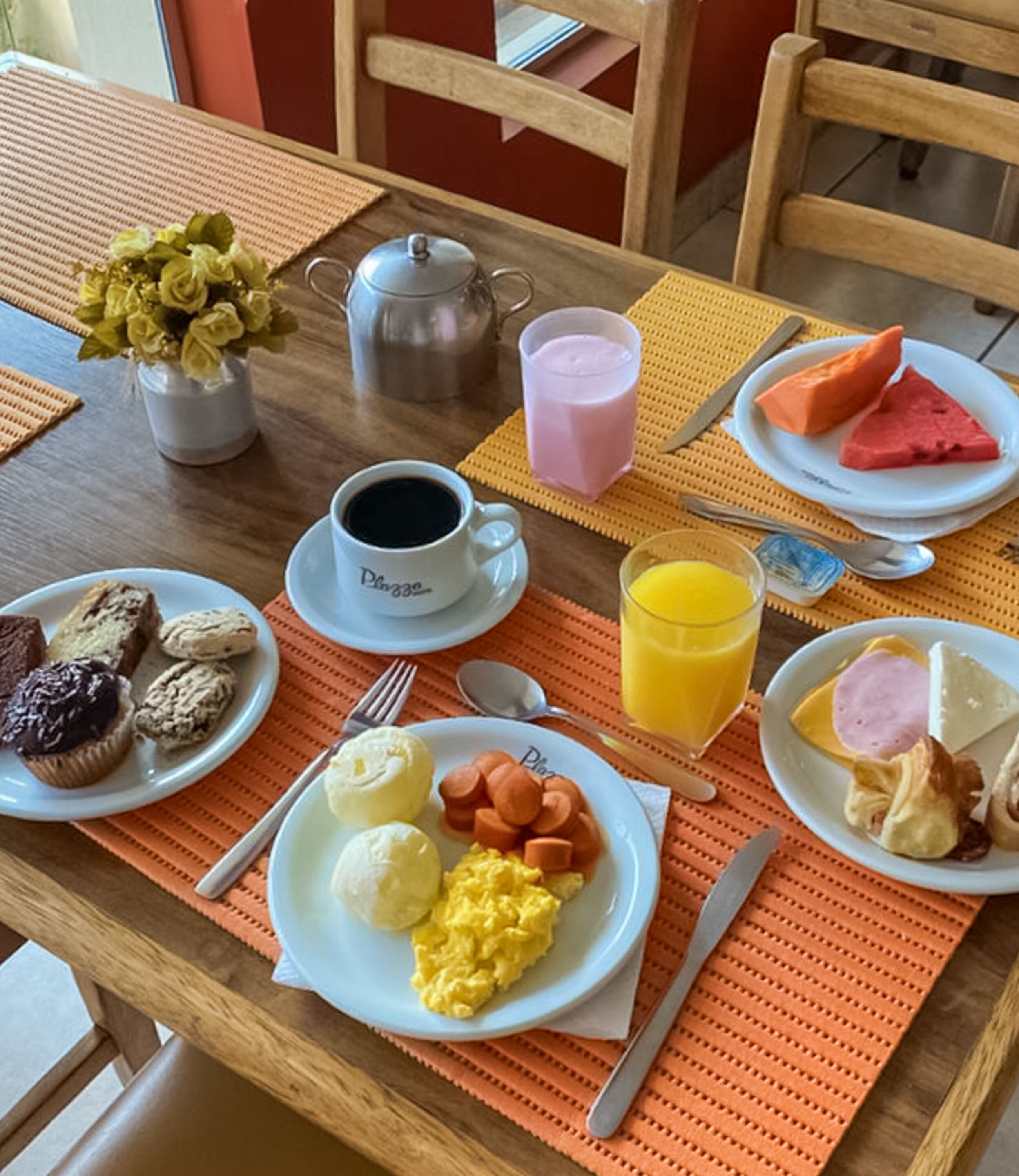 Ein Frühstückstisch mit Eiern, Würstchen und Toast, einer Kaffeetasse, einem Saftkrug und einem Teekessel.