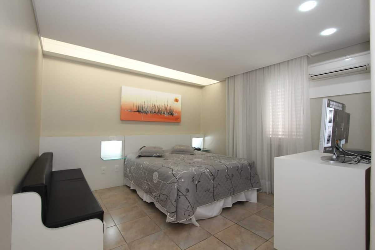 Ein modernes Hotelzimmer mit Bett, Schreibtisch, Computer und einem Bild an der Wand.