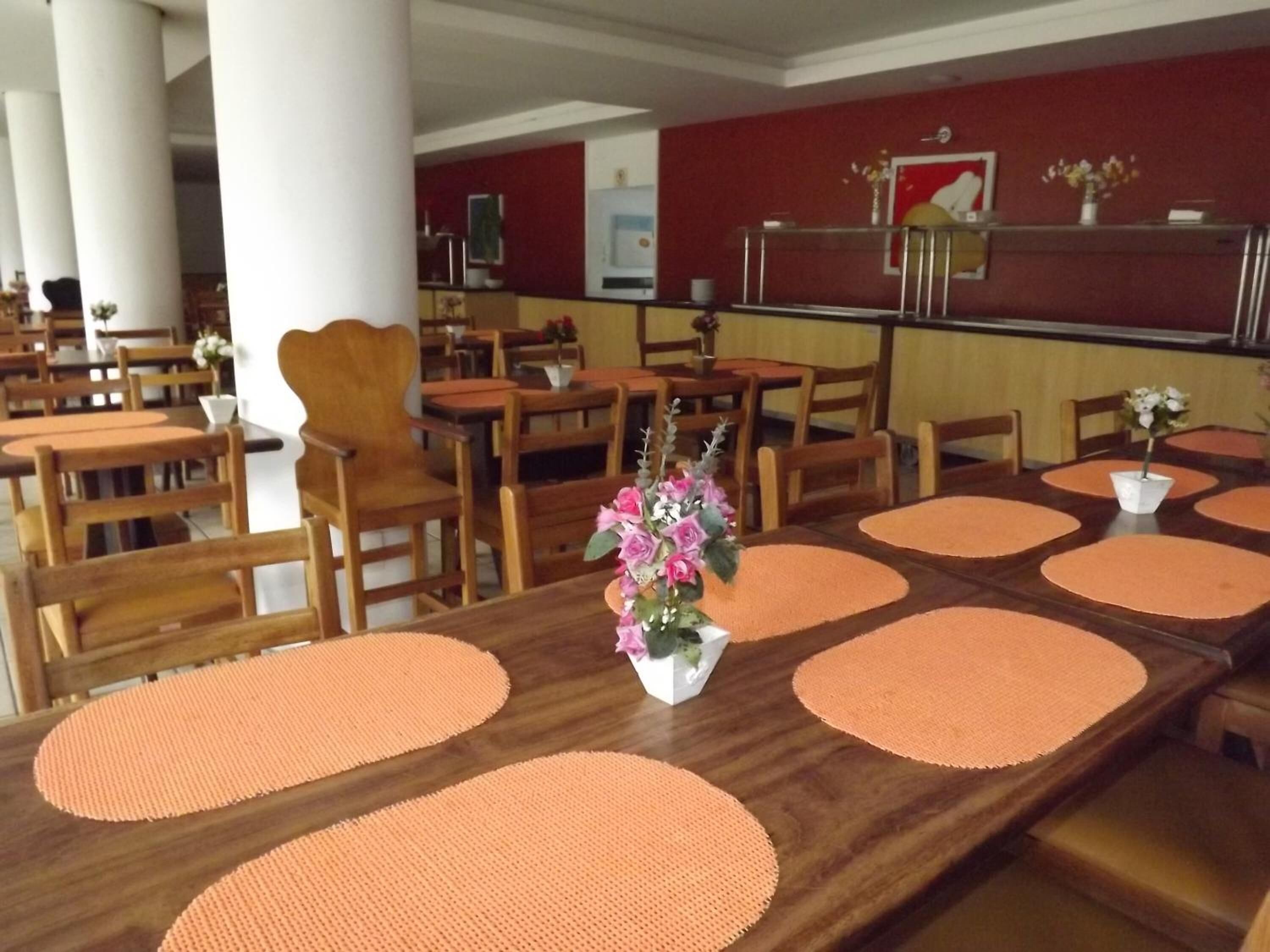 En restaurant med træborde og stole, en central receptionsdisk og en rød væg med et indrammet billede.