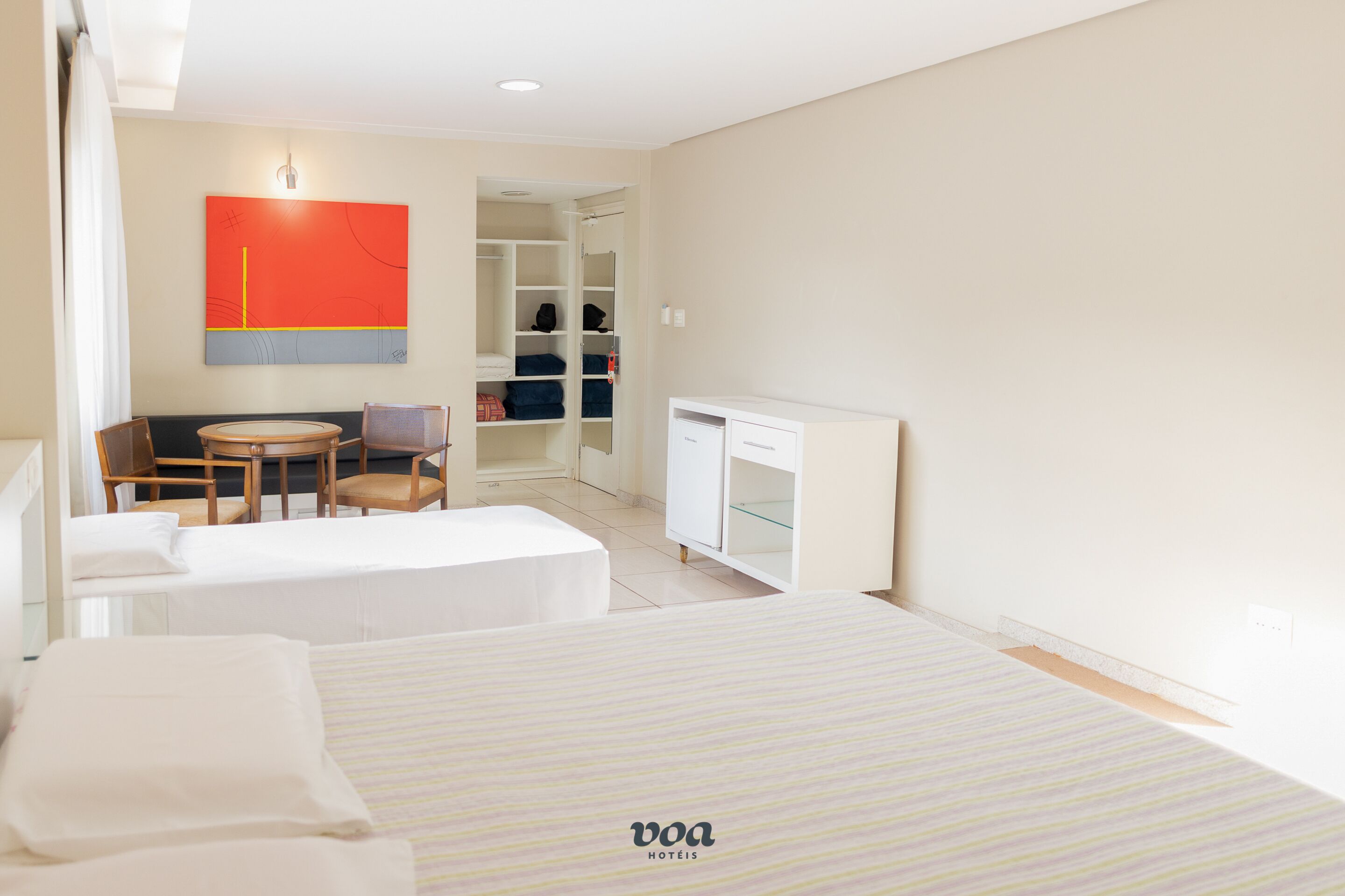 A hotel room with two beds, a desk, a chair, and a wardrobe.