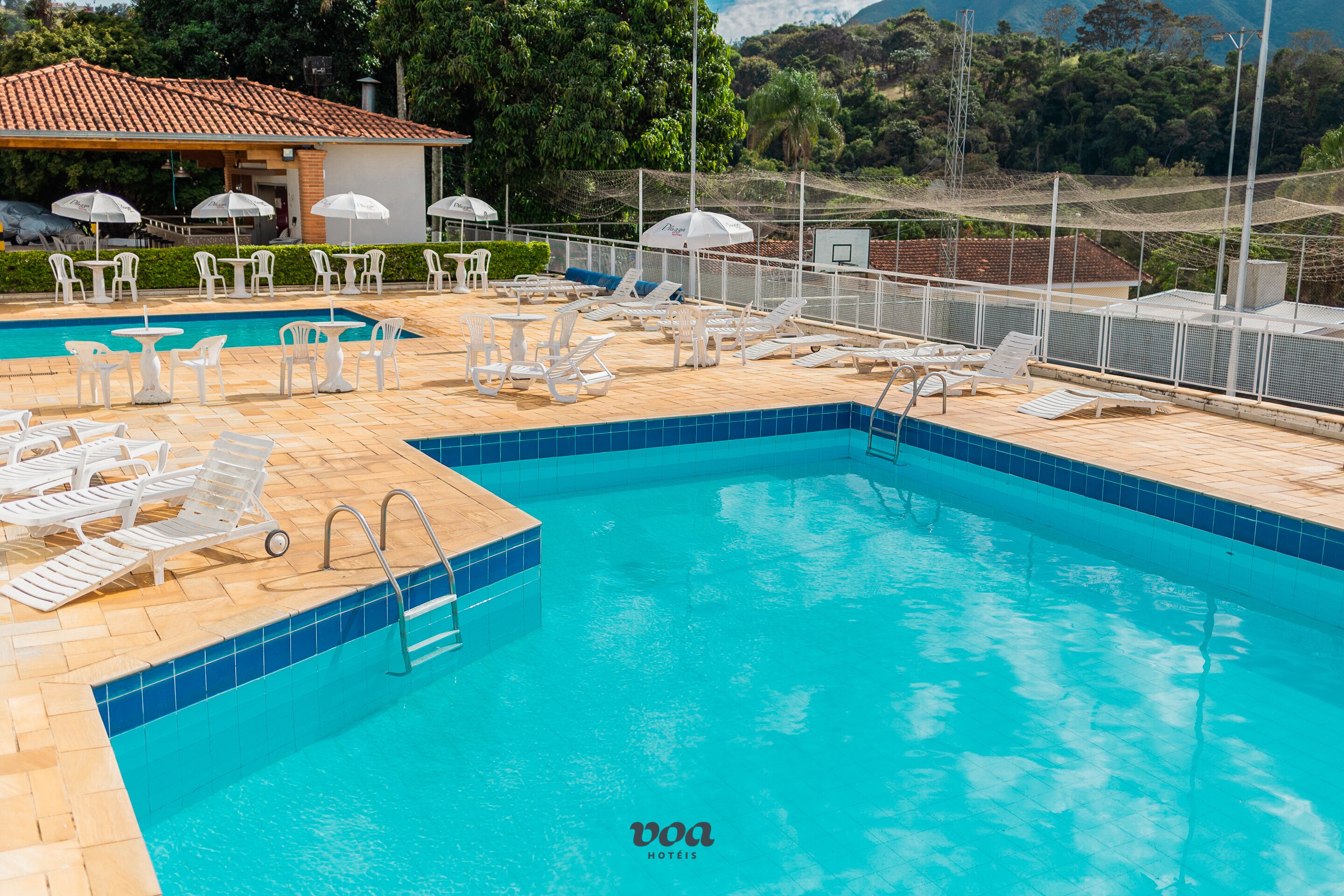 A swimming pool with lounge chairs and umbrellas, surrounded by a fence and trees in the background.