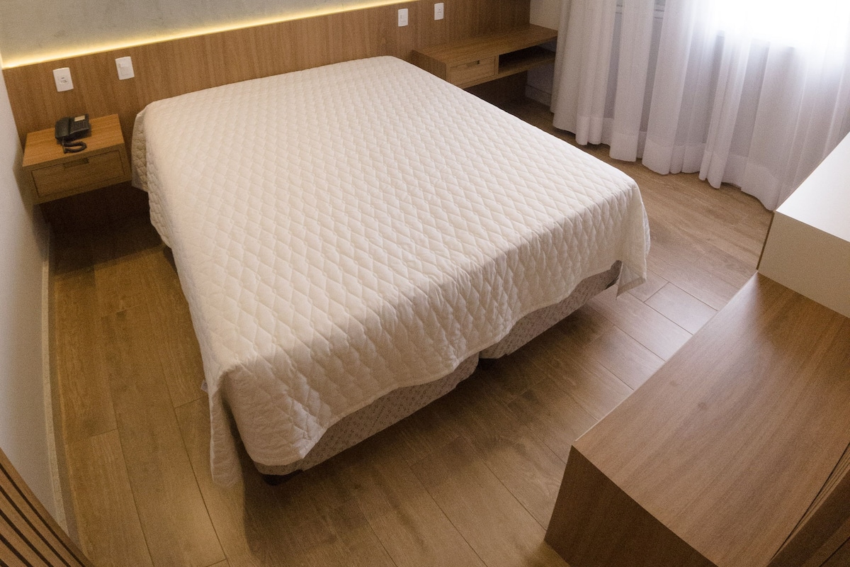 Ein modernes Schlafzimmer mit einem großen Bett, einem Holzkopfteil, Nachttischen und einer eingebauten Ablagefläche.