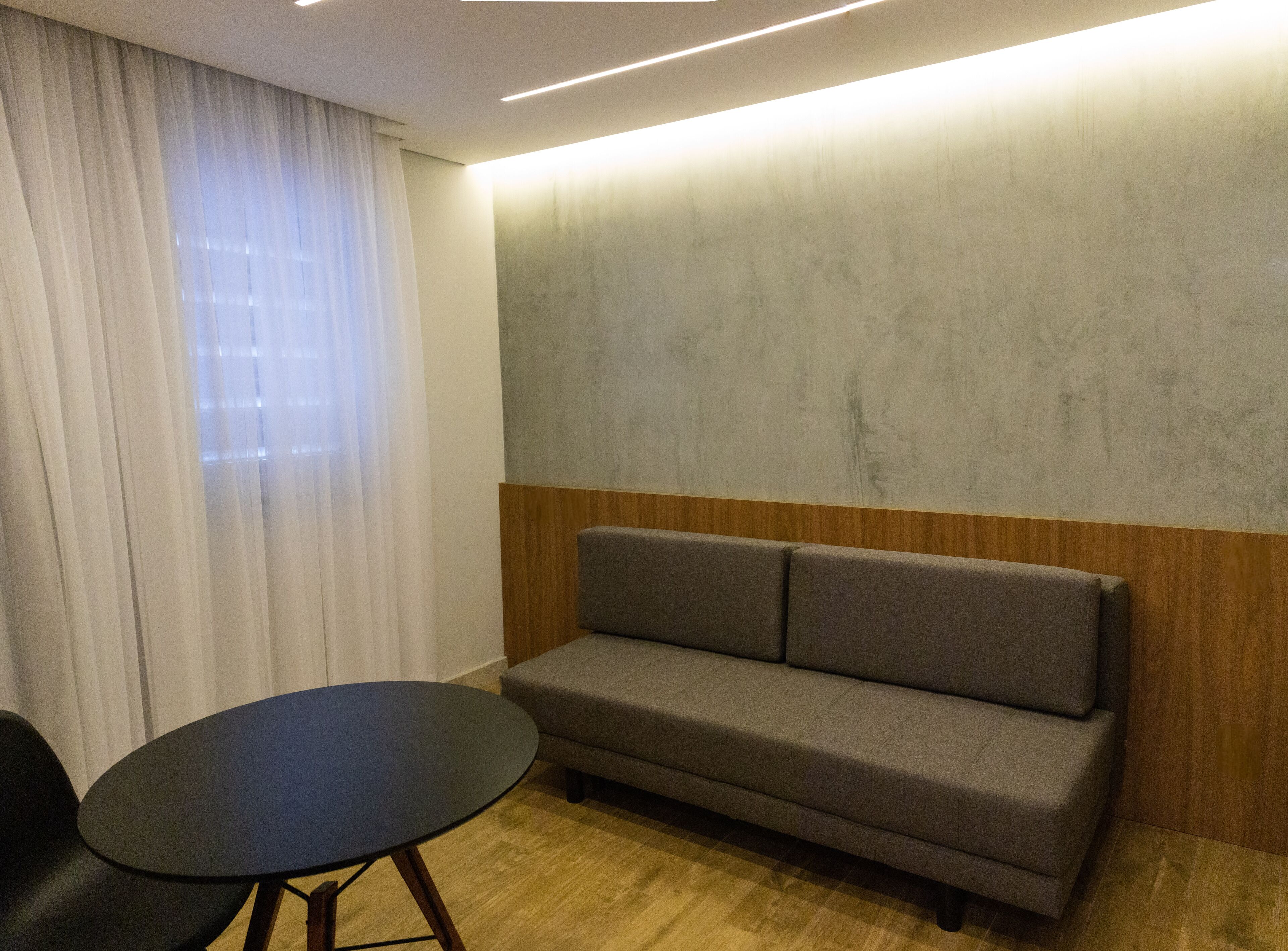 Una habitación moderna con un sofá gris, una pequeña mesa redonda y un revestimiento de pared de madera.