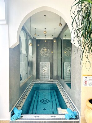 Una piscina con un diseño geométrico de azulejos, una pared con un panel decorativo y luces esféricas colgantes.
