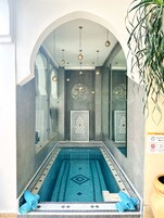 A swimming pool with a geometric tile pattern, a wall with a decorative panel, and hanging spherical lights.