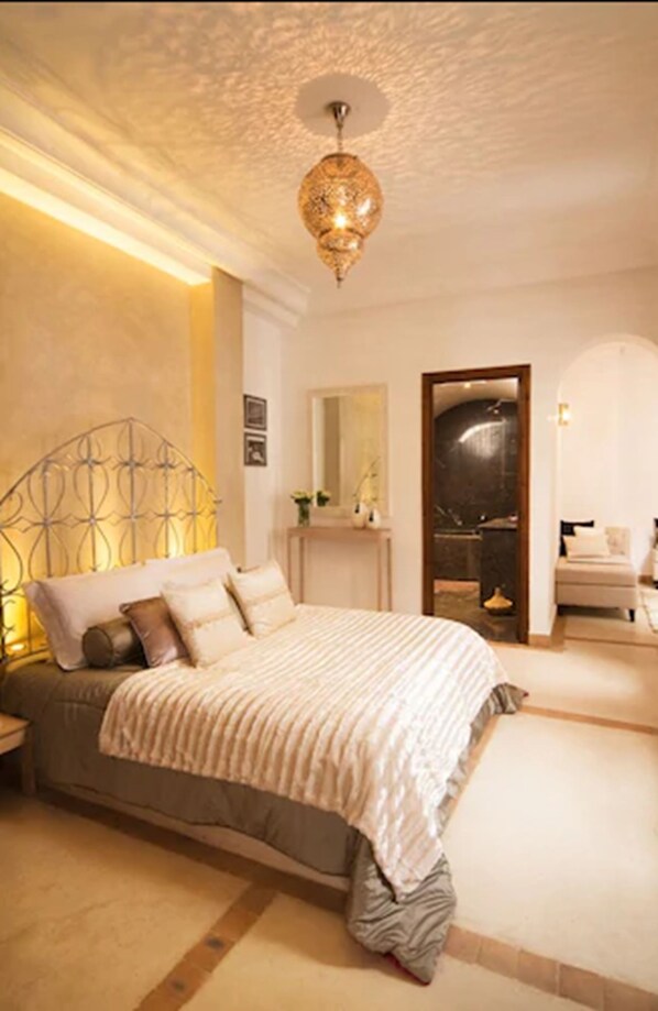 A bedroom with a bed, a nightstand, a mirror, and a door leading to a bathroom. - Riad Chayma - Adults Only (Marrakech)