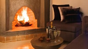 A cozy living room with a fireplace, a sofa, and a table with a bottle and glasses. - Riad Chayma - Adults Only (Marrakech)
