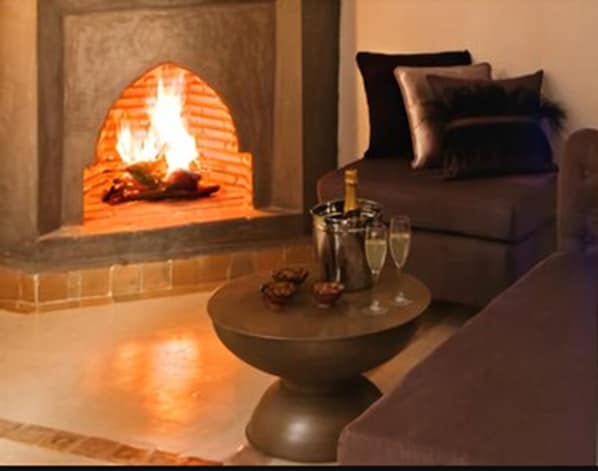 A cozy living room with a fireplace, a sofa, and a table with a bottle and glasses. - Riad Chayma - Adults Only (Marrakech)