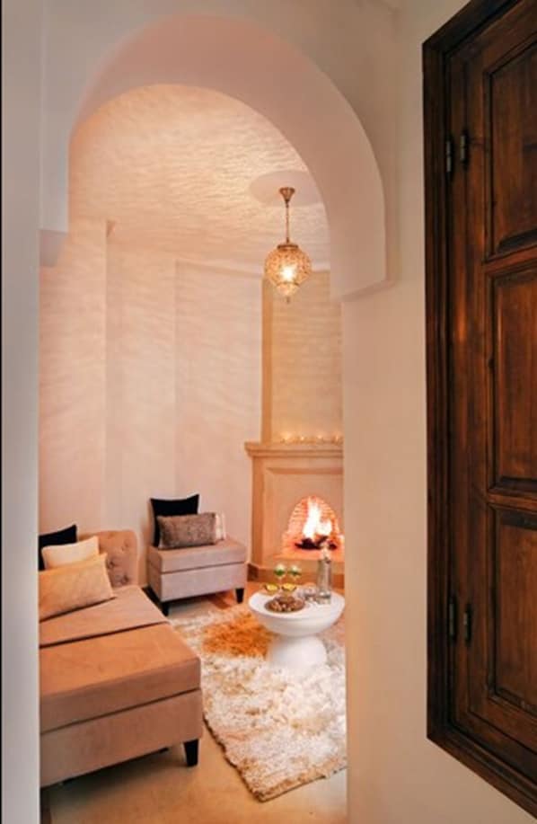 A cozy living room with a fireplace, a sofa, and a coffee table. - Riad Chayma - Adults Only (Marrakech)