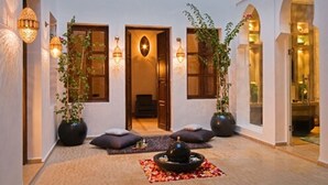 A traditional interior with a central seating area, a doorway leading to another room, and wall-mounted lighting fixtures. - Riad Chayma - Adults Only (Marrakech)