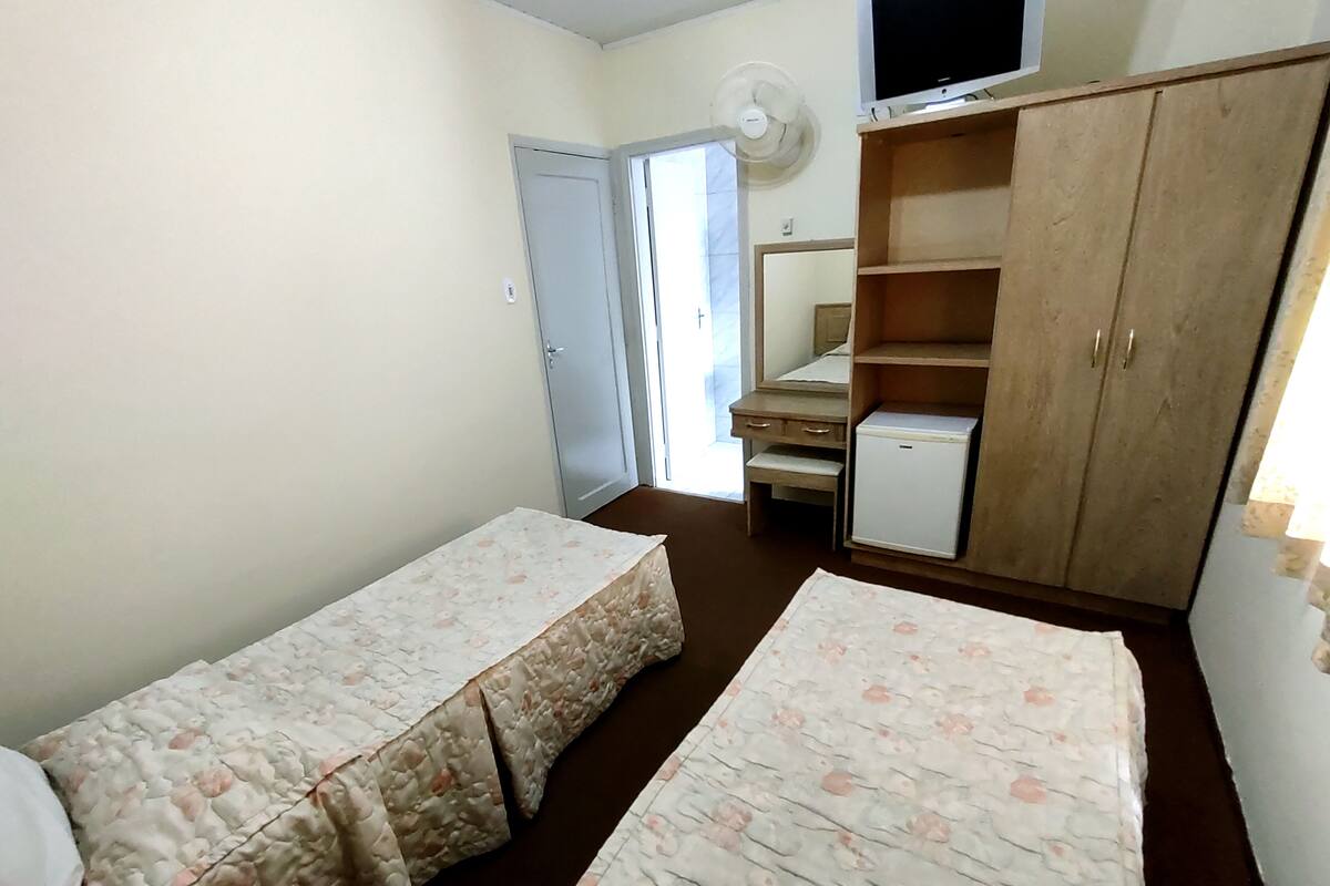 Una habitación pequeña y sencilla con dos camas individuales, un armario de madera, un escritorio pequeño y una televisión.