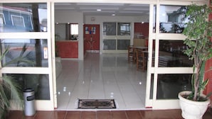 A hotel lobby with a reception desk, a dining area, and a large potted plant. - Pousada Águas de Lindóia (Águas de Lindóia)