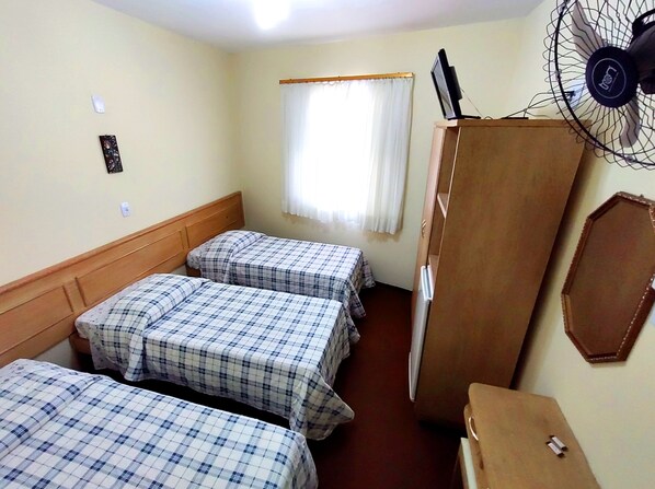 Una habitación con tres camas, un armario de madera, un ventilador y una ventana con cortinas.