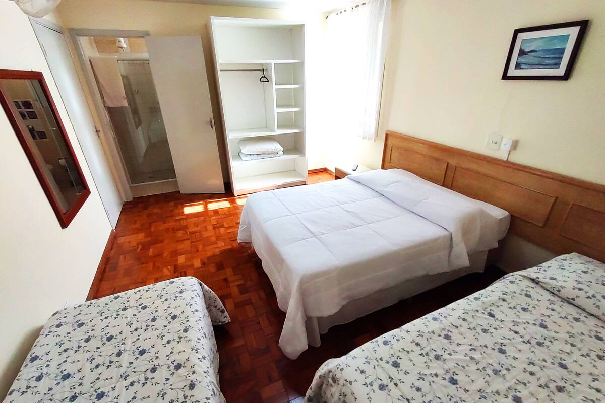 Una habitación con dos camas, suelo de madera, un armario blanco y un baño visible a través de una puerta abierta.