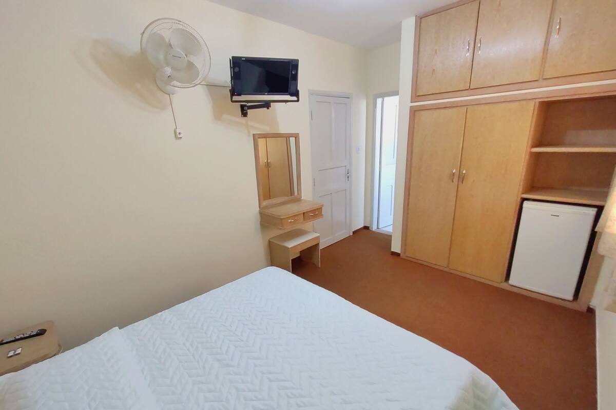 Un dormitorio con cama, televisor montado en la pared, refrigerador pequeño y armario.