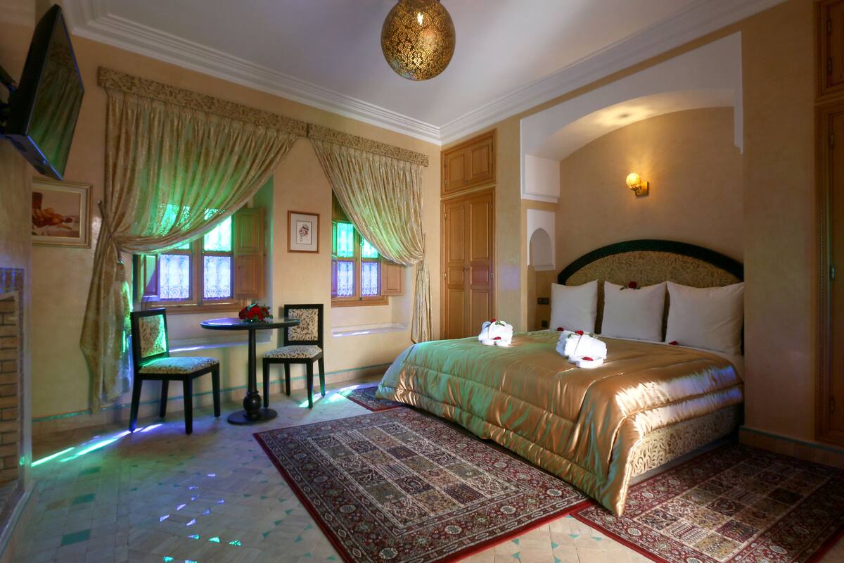 A hotel room with a large bed, a desk with a chair, a small table, and a window with curtains.