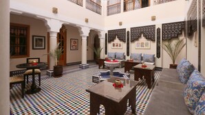 Une cour spacieuse avec un sol à carreaux, un coin salon avec des canapés et une table basse, et un balcon doté d’une balustrade.