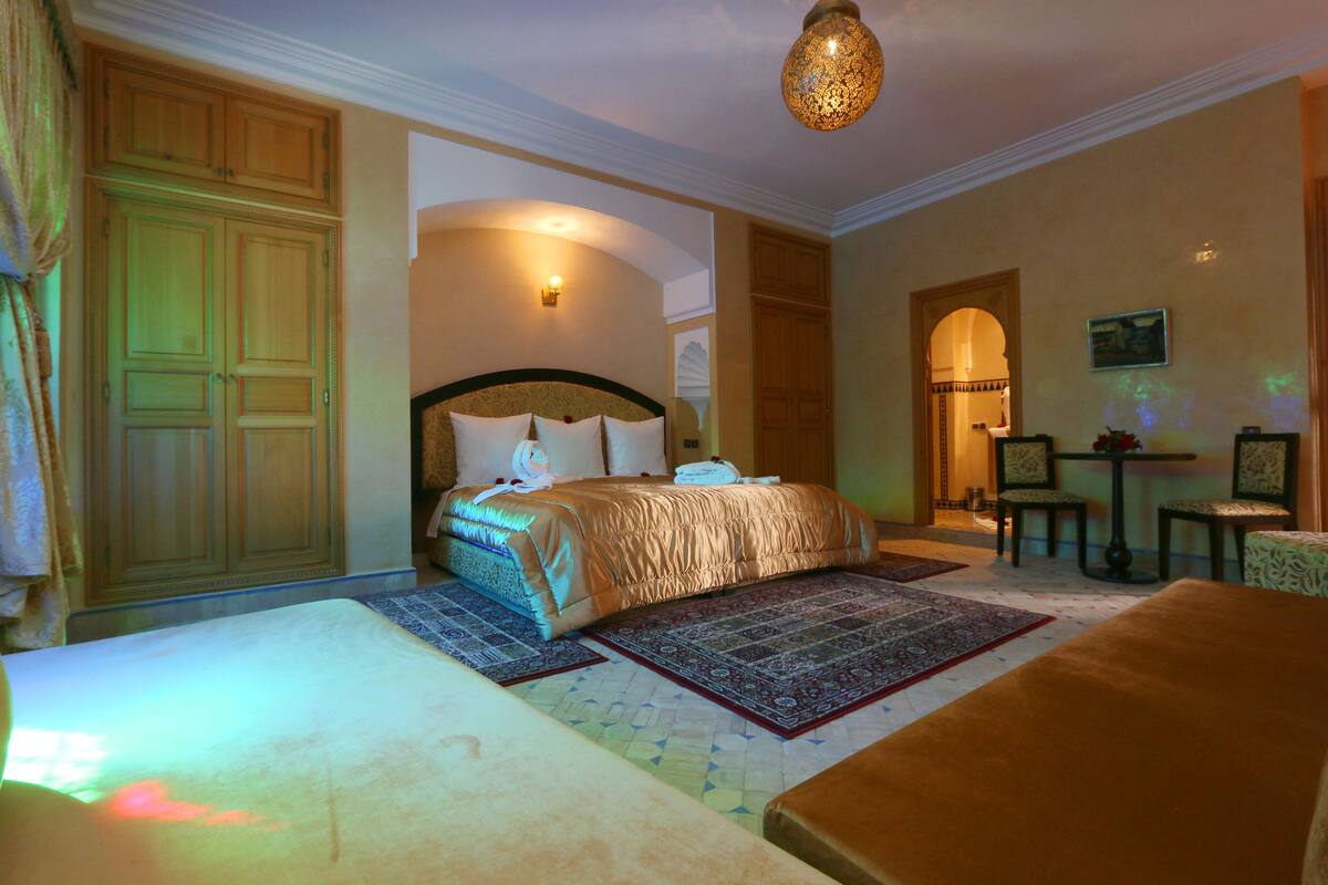 A spacious bedroom with a large bed, a sitting area with a table and chairs, and a wardrobe.