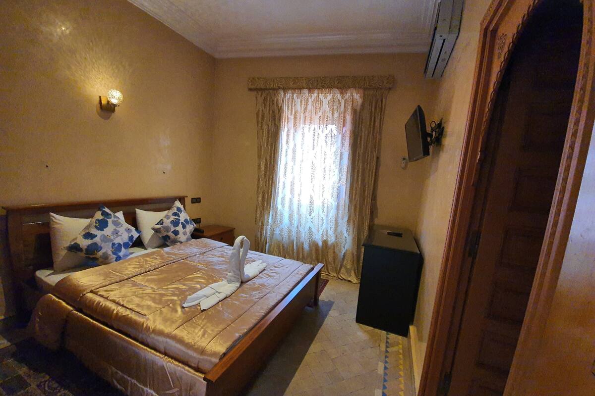 A hotel room with a large bed, a nightstand, a lamp, a window with curtains, and a door.