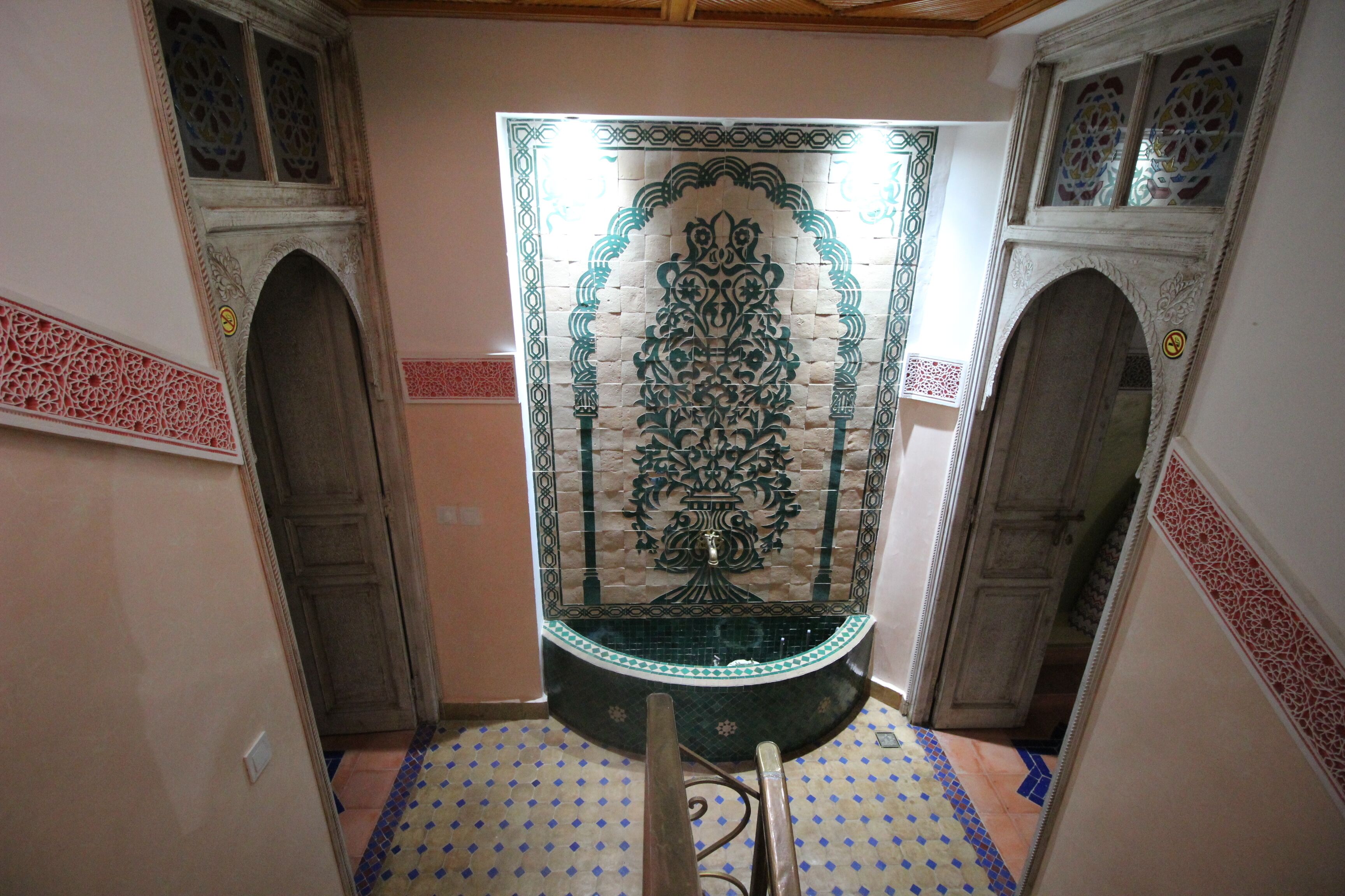 Un pasillo con un panel decorativo en la pared, puertas de madera y baldosas de suelo con diseños.