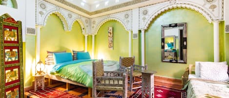 A room with a bed, two chairs, a small table, and a decorative mirror.