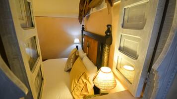 Una habitación de hotel estrecha con una cama, una mesita de noche con una lámpara y una ventana con cortinas.