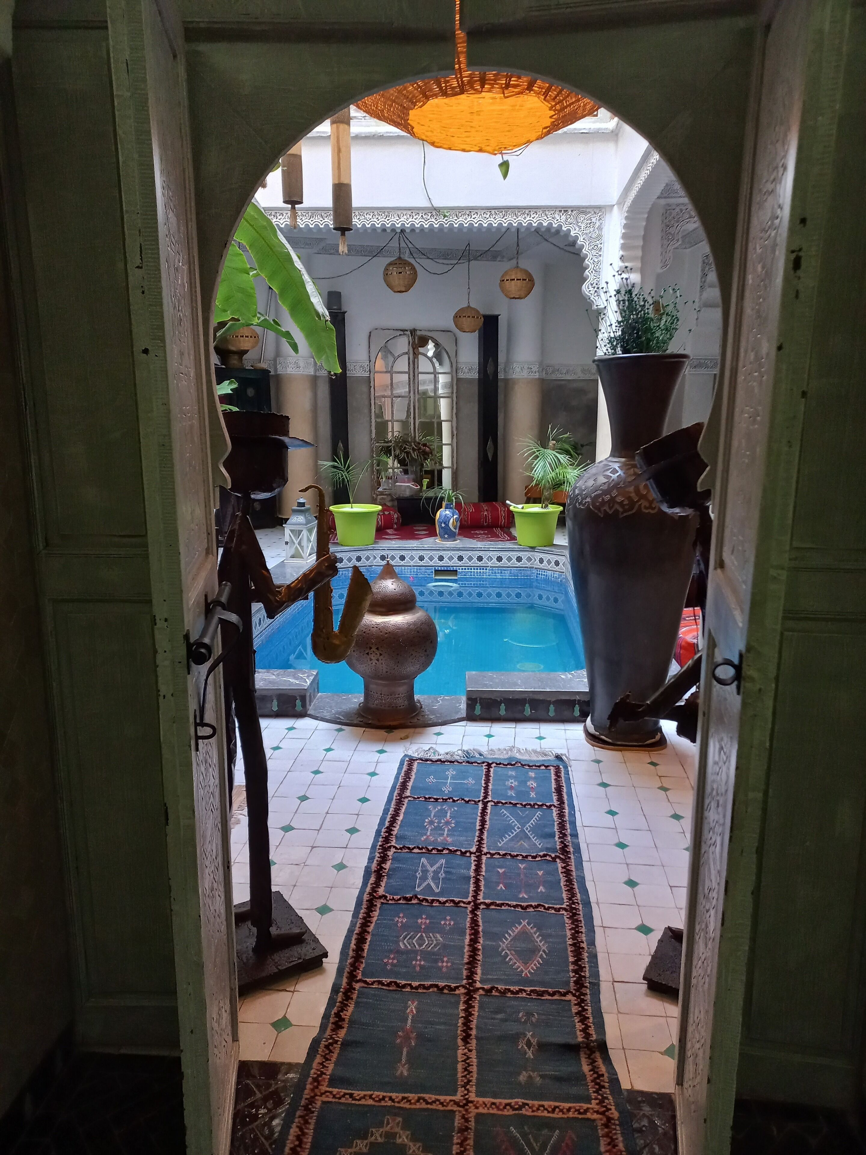 An arched doorway leading to a courtyard with a pool, potted plants, and a decorative rug.