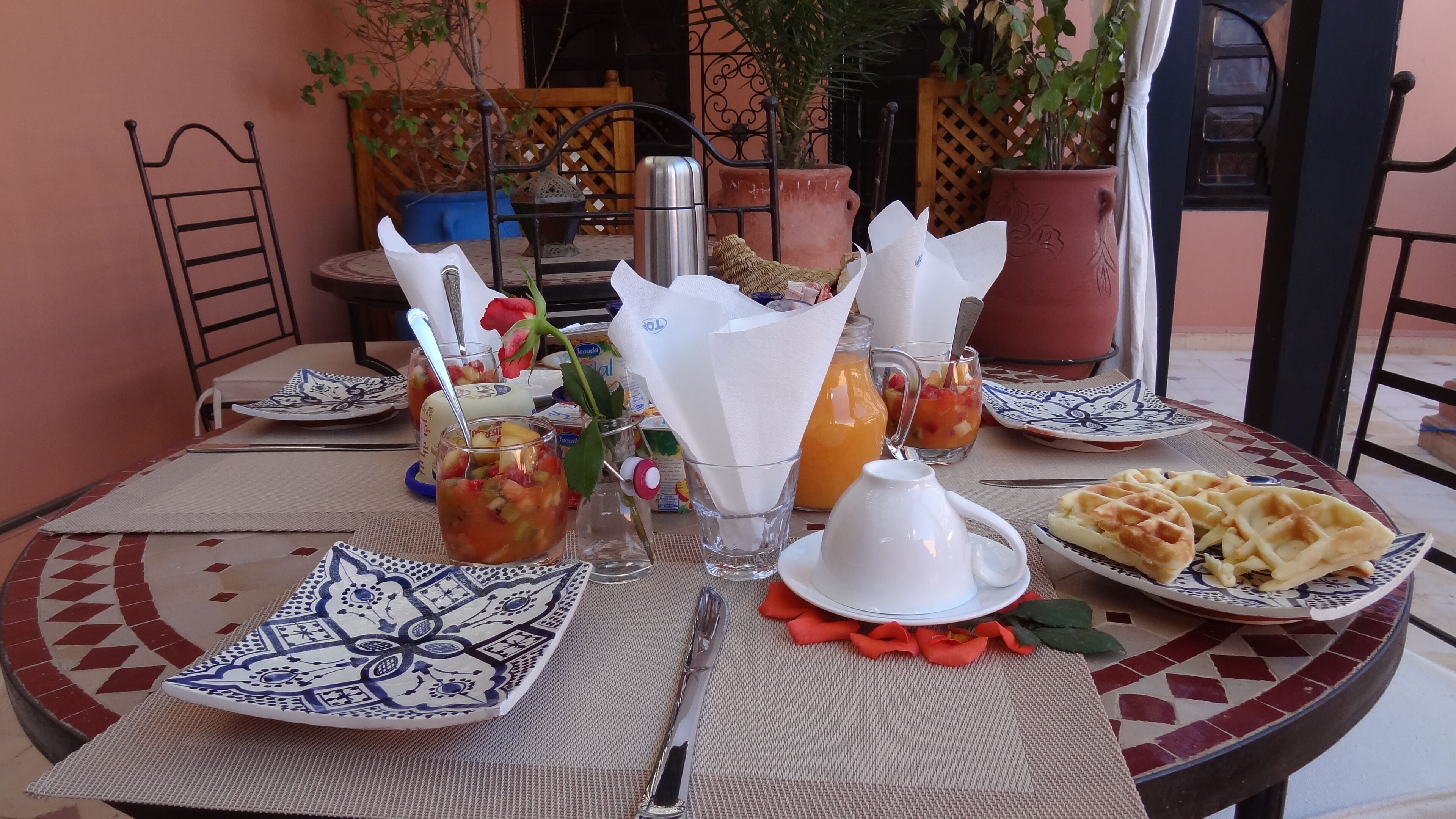 A breakfast table set with plates, glasses, a thermos, and a waffle plate.