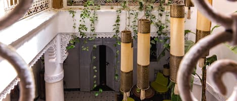 Un interior tradicional con barandillas de metal ornamentadas, plantas colgantes y un suelo con diseño.