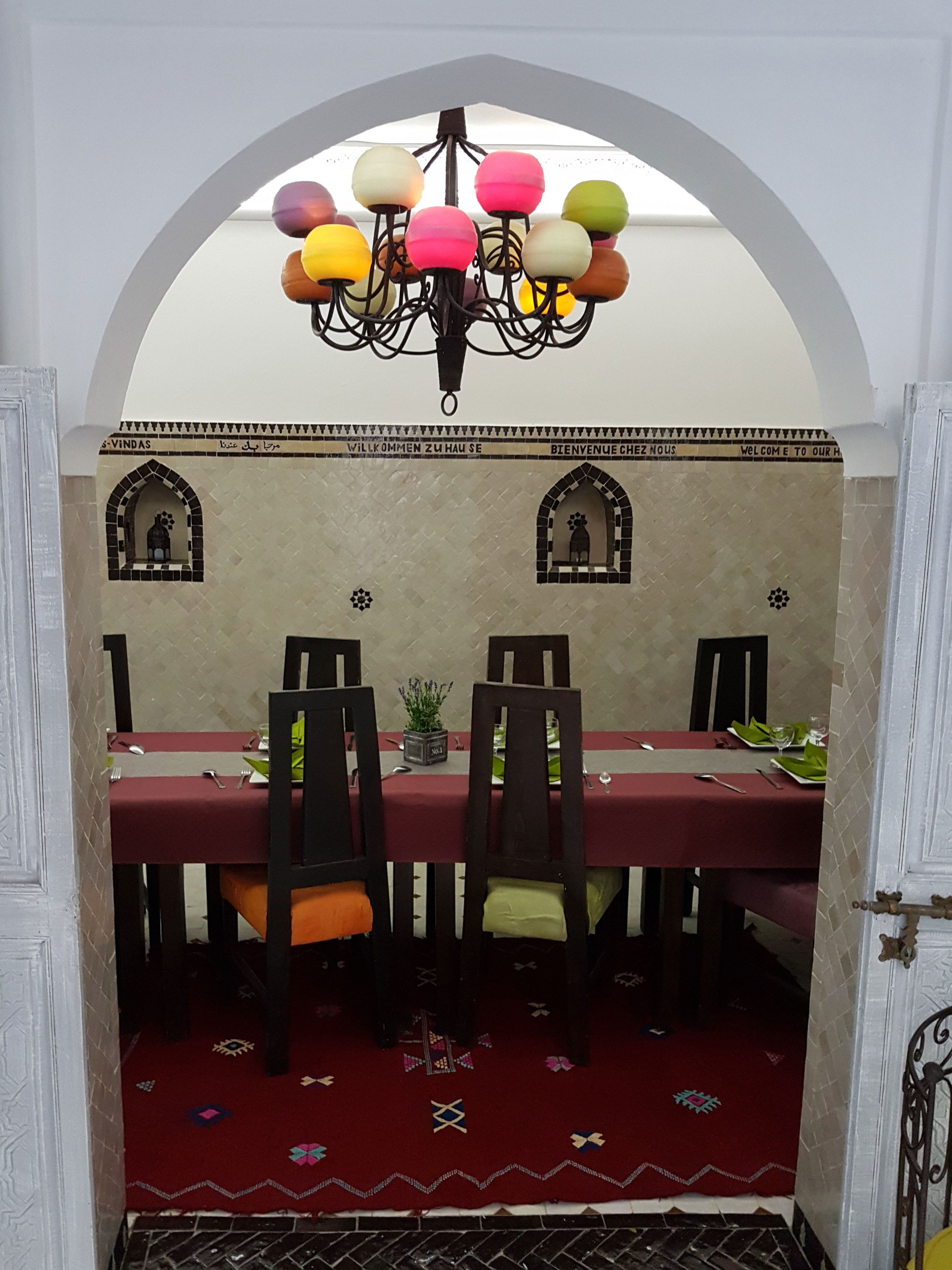 Un espace repas avec une table rouge, des chaises noires et un lustre orné de sphères lumineuses aux couleurs vives.