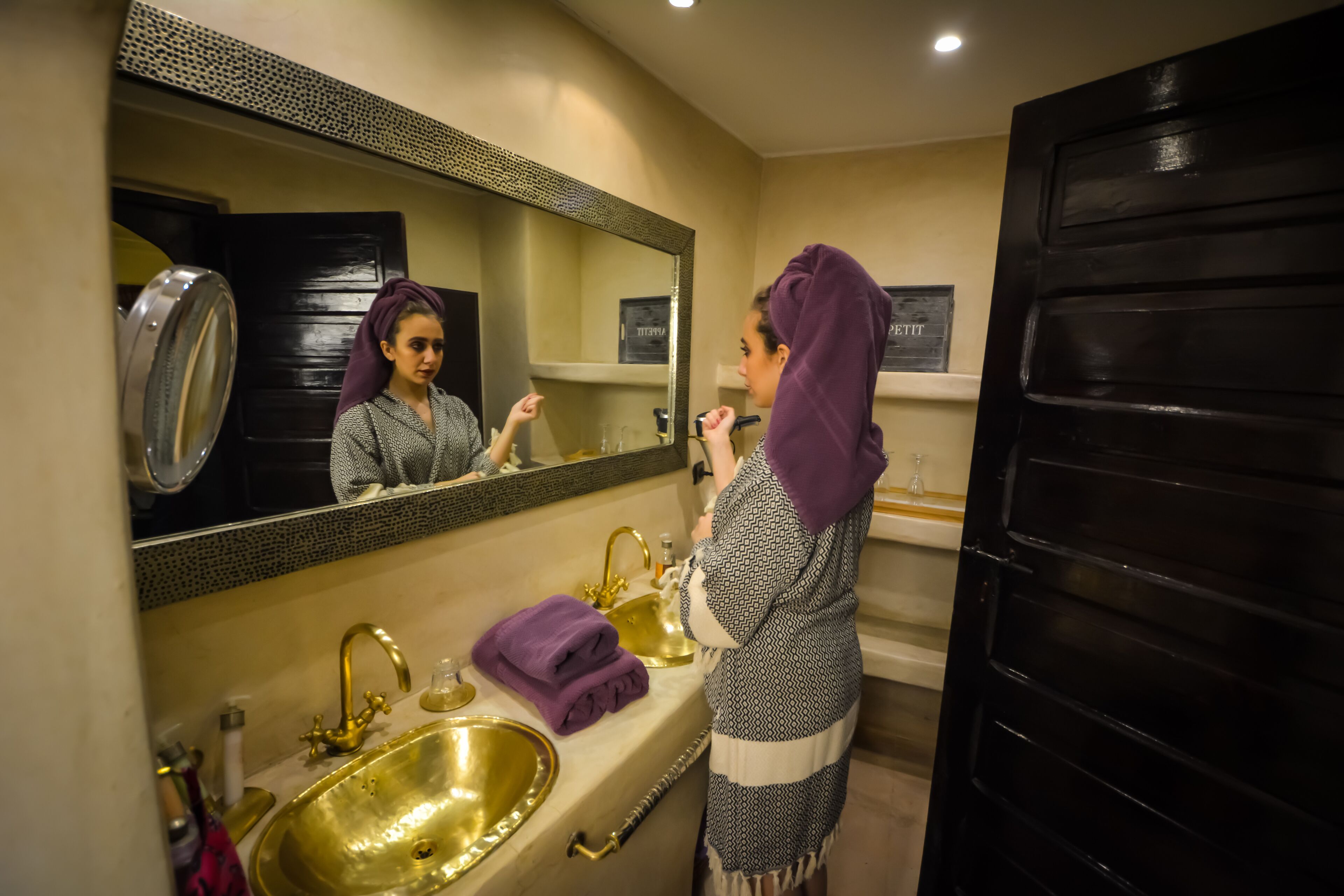 Un baño con un lavabo dorado, un espejo grande y una puerta negra.
