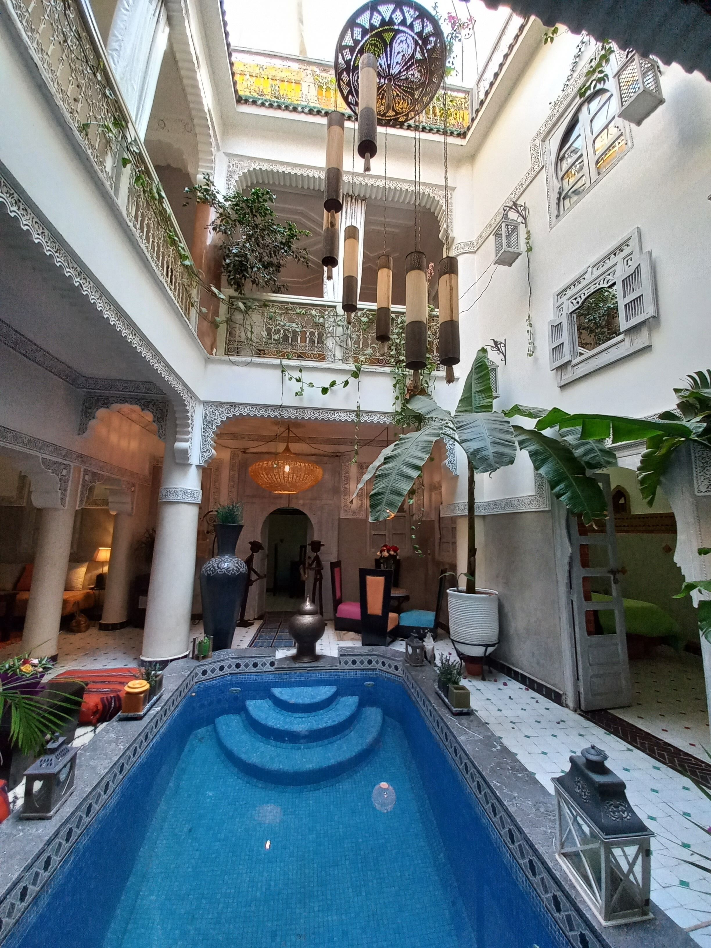 Una piscina interior con suelo de baldosas, rodeada de columnas y una fuente decorativa.