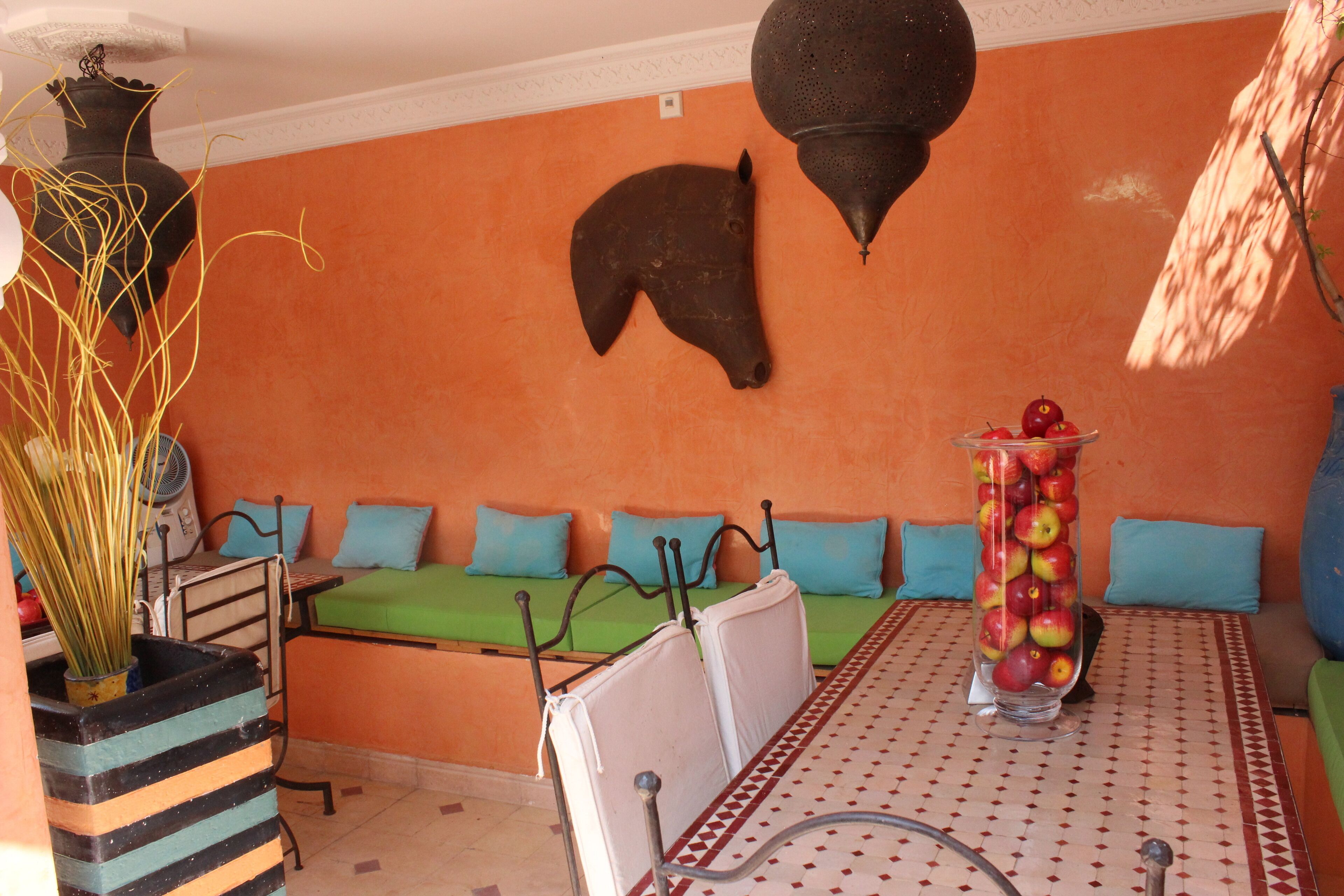 Una habitación con un sofá verde, una estructura metálica para cama, una mesa con un jarrón de manzanas y un adorno colgado en la pared.