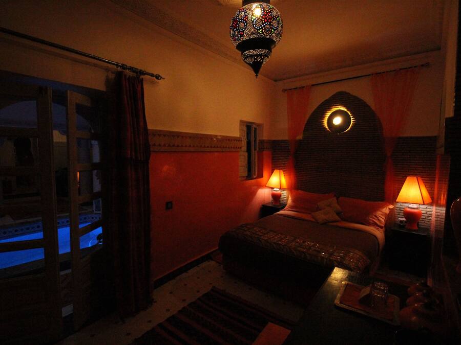 Una habitación tenuemente iluminada con una cama, dos lámparas de noche, una lámpara decorativa en el techo y una ventana con cortinas.