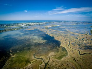 An aerial view of a coastal landscape with a river meandering through a marshy area, surrounded by water bodies and distant urban areas. - Agriturismo La Barena (Jesolo)