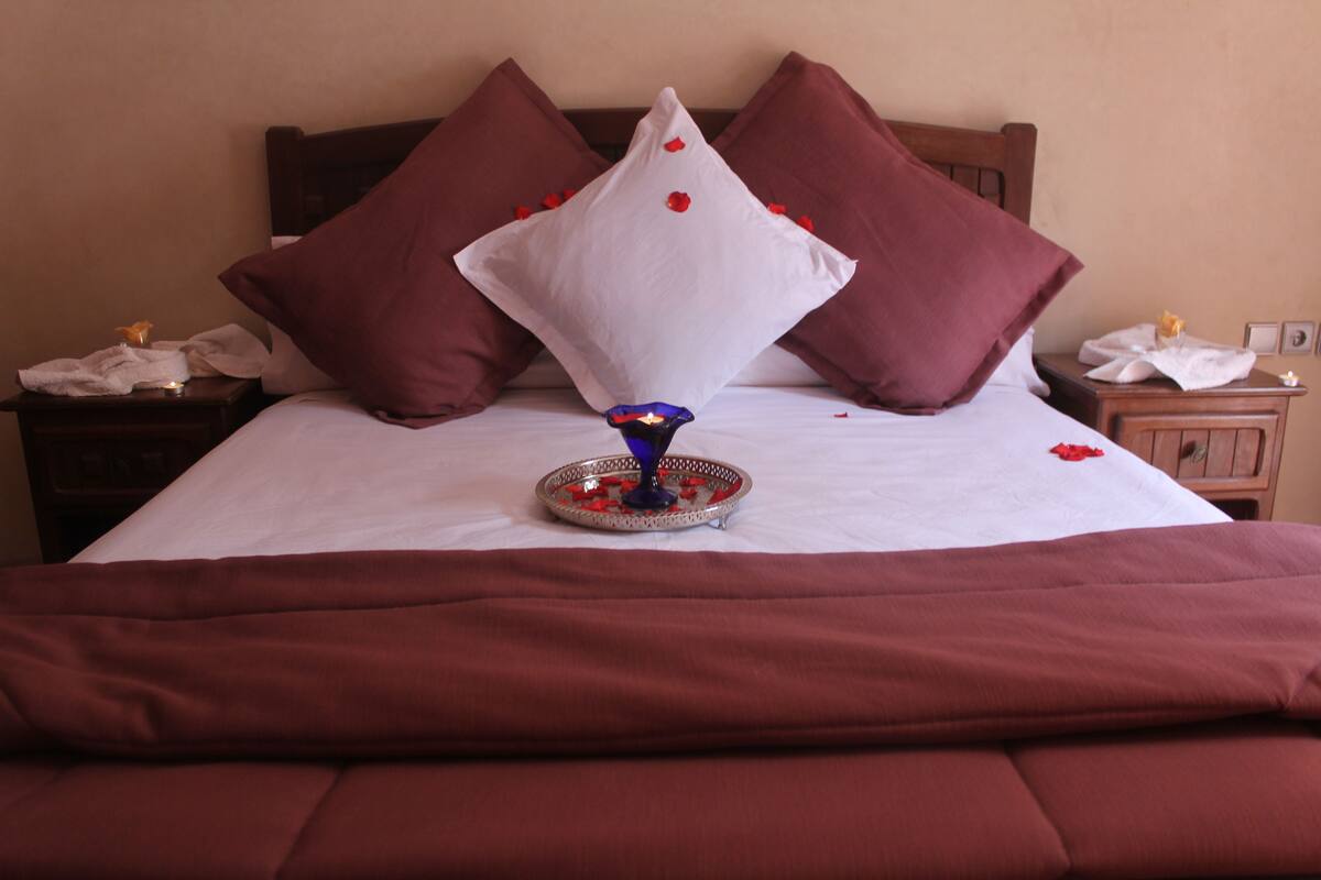 A neatly made bed with a white and brown color scheme, a decorative tray with a candle, and a wooden headboard.