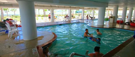 An indoor swimming pool with people swimming and lounging.