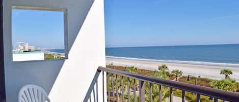 A balcony with a white chair, a view of the beach, and a Ferris wheel in the distance.